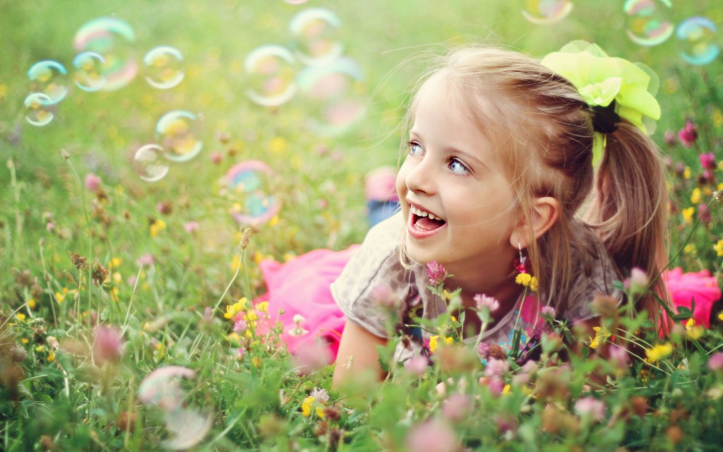 Sweet, happy, smiling six year old girl laying on a grass in a park playing with bubbles and laughing